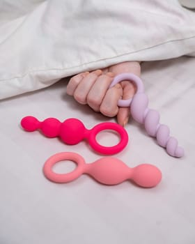 A woman chooses anal beads from a set while lying in bed