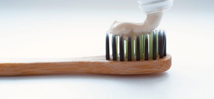 Stylish bamboo toothbrush on a light background in the bathroom with a toothpaste from a tube, close-up macro view.