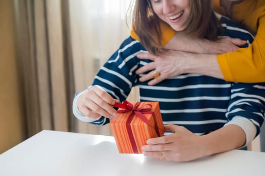 The grandmother gives a nice gift to her daughter or granddaughter, gently hugs a dear person, girl is happy and accepts a surprise with a joyful expression on her face. Family happiness and harmony.