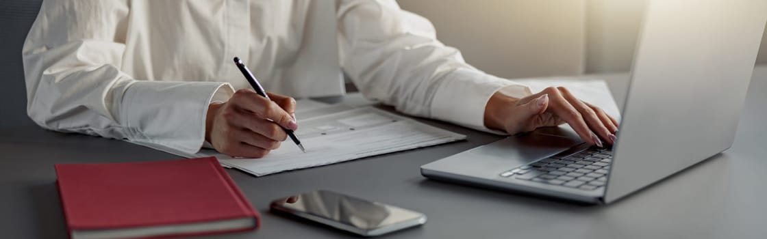 Close up of business woman working laptop and making notes sitting in office. Blurred background