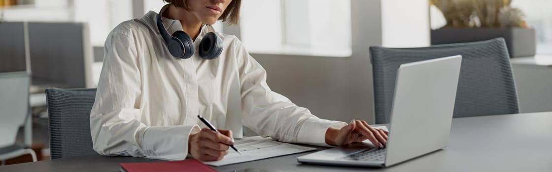 Business woman working laptop and making notes while sitting in modern office. Blurred background