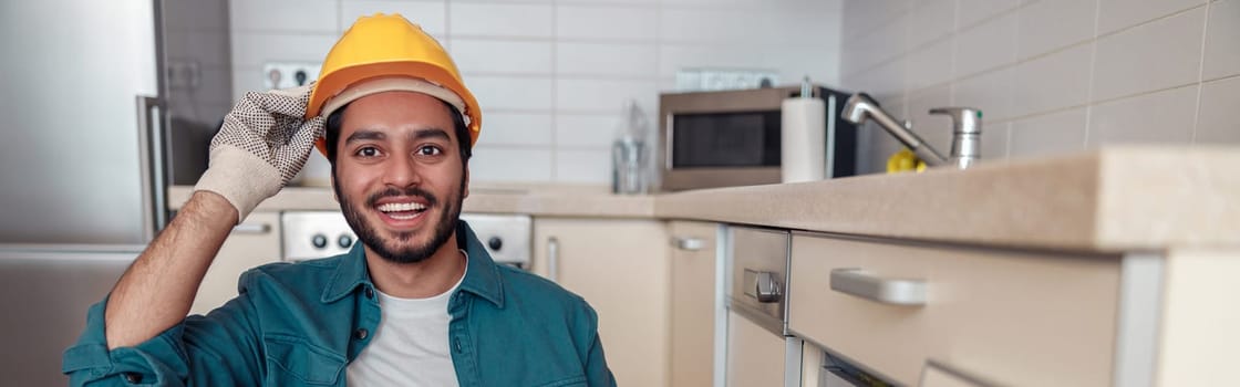 Male worker in uniform is assembling furniture on kitchen. Repair concept. High quality photo