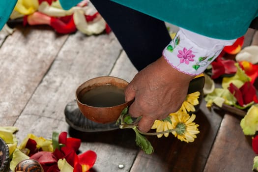 indigenous woman picking up a bowl full of liquid to perform a ritual surrounded by yellow and red flowers. High quality photo