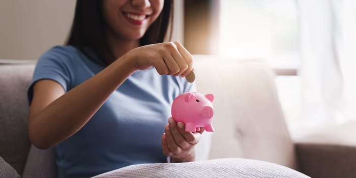 Young asian woman hand putting coins in pink piggy bank for account save money. saving money, retirement fund. investment, finance accounting.