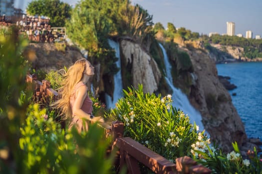 Beautiful woman with long hair on the background of Duden waterfall in Antalya. Famous places of Turkey. Lower Duden Falls drop off a rocky cliff falling from about 40 m into the Mediterranean Sea in amazing water clouds. Tourism and travel destination photo in Antalya, Turkey. Turkiye.