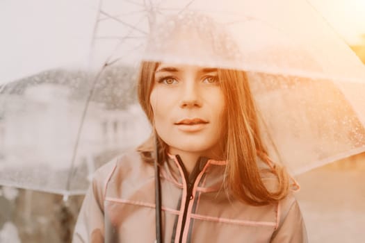 Woman rain park. Happy woman portrait wearing a raincoat with transparent umbrella outdoors on rainy day in park near sea. Girl on the nature on rainy overcast day