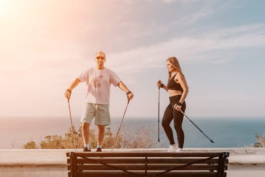 Happy Middle aged couple or friends practicing nordic walking in park near sea. Mature couple with trekking poles walking, practicing Nordic walking outdoors. Aging youthfully and sport concept.