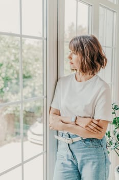 Office window woman. Business woman standing in the office with her arms crossed near the window. Dressed in a white T-shirt and jeans