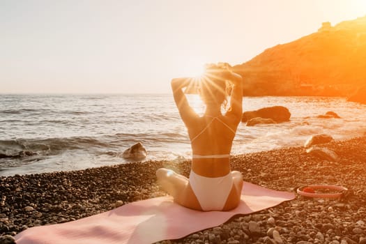 Young woman in swimsuit with long hair practicing stretching outdoors on yoga mat by the sea on a sunny day. Women's yoga fitness pilates routine. Healthy lifestyle, harmony and meditation concept.