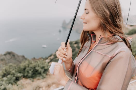 Woman rain park. Happy woman portrait wearing a raincoat with transparent umbrella outdoors on rainy day in park near sea. Girl on the nature on rainy overcast day