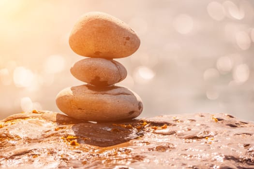 Balanced Pebbles Pyramid on the Beach on Sunny Day and Clear Sky at Sunset. Blue Sea on Background Selective focus, zen stones on sea beach, meditation, spa, harmony, calm, balance concept.