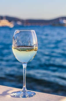 A glass of white wine with a reflection of the coast in it. Relax at a table in a restaurant by the sea. High quality photo