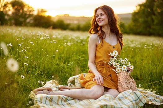 beautiful woman, in a summer orange dress enjoys nature while sitting in a chamomile field. High quality photo