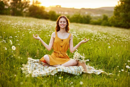 a woman in a chamomile field meditates holding her hands on her chest while sitting on a plaid. High quality photo