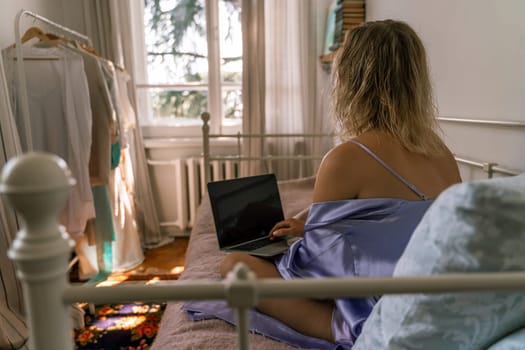 A top view of a woman in a purple nightgown using a laptop on a bed, suggesting that she is working or studying from the comfort of her own home