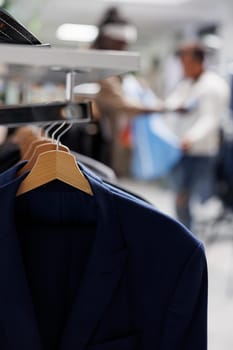 Jackets hanging on rack in trendy clothing store for sale with blurred background. Casual modern blazers from new collection on hangers in department shopping mall close up selective focus