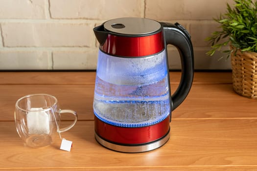 a fashionable tea cup with double glass walls and a modern electric transparent teapot with bubbling water and blue neon lighting on the table close-up