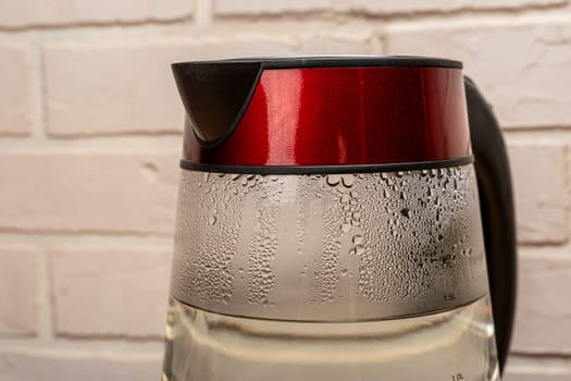 new modern electric kettle made of heat-resistant glass close-up with condensation drops on the walls against a light brick wall