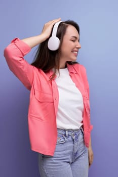 optimistic dancing brunette young woman in a shirt and jeans listens to her favorite music on headphones.