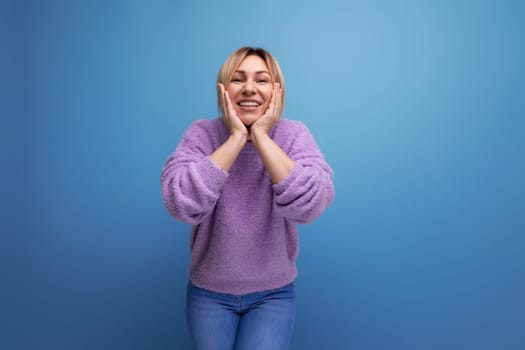 joyful energetic blond young woman consultant in purple sweater happy on blue background with copy space.