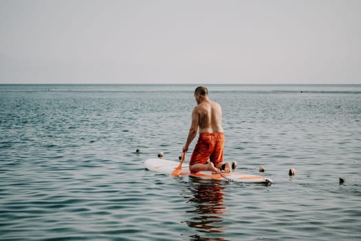 Active mature male paddler with his paddleboard and paddle on a sea at summer. Happy senior man stands with a SUP board. Stand up paddle boarding - outdor active recreation in nature