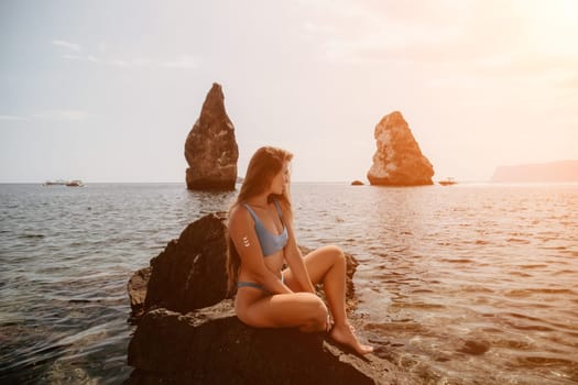 Woman travel sea. Young Happy woman in a long red dress posing on a beach near the sea on background of volcanic rocks, like in Iceland, sharing travel adventure journey