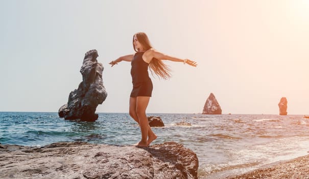 Woman travel sea. Young Happy woman in a long red dress posing on a beach near the sea on background of volcanic rocks, like in Iceland, sharing travel adventure journey