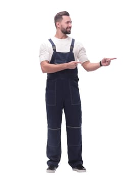in full growth. smiling man in overalls pointing to a copy of the space . isolated on white