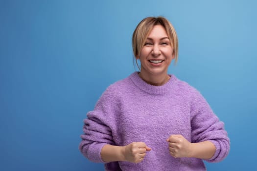 energetic blond young woman in purple hoodie on blue background with copy space.