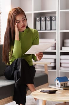 Stressed woman sits on sofa at home, studying and analyze house bills and submitting tax forms..