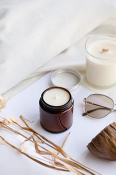 Soy wax aroma candle in brown jar on bed , with fashion glasses. Candle mockup design. Mockup soy wax candle in natural style.