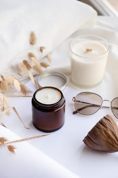 Soy wax aroma candle in brown jar on bed , with fashion glasses. Candle mockup design. Mockup soy wax candle in natural style.