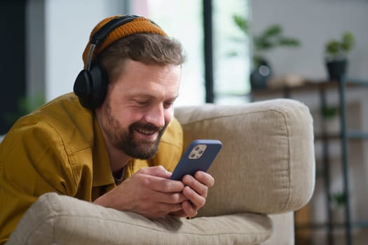 Happy man laying on sofa home, smiling while chatting online on mobile phone through messaging app. Relaxed and casual atmosphere, showcasing modern technology for communication and socializing. High quality photo