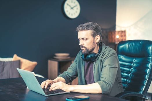 Man sitting at desk home, typing on laptop and chatting online through messaging app. He dressed in casual clothing and surrounded by technology, with wireless mobile phone router visible in the background. This image is perfect for representing remote work, telecommuting, or the modern workplace. High quality photo