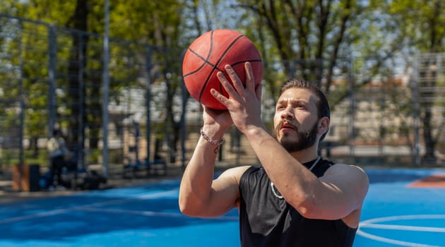 Athletic lebanese man in sportswear playing basketball game, successfully throws ball into the basket ring. Young guy on urban city summer court. Fitness routine on sports field. Motivation. Outdoors