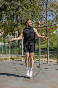 Athletic lebanese man in sportswear skipping rope. Young middle eastern arabian guy doing jumping exercises on playground. Sports crossfit, fitness routine, workout. Strength motivation. Outdoors