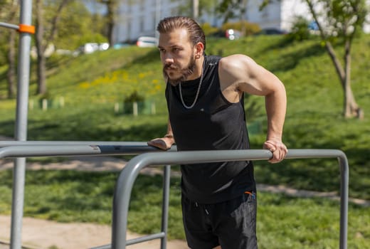 Athletic lebanese man in sportswear practicing dips on parallel bars, training triceps. Young middle eastern guy on playground. Sports health fitness routine, workout. Strength motivation. Outdoor gym
