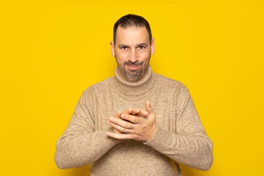 Cunning hispanic man rubbing his hands on isolated yellow background, person rubbing his hands planning something, evil concept.