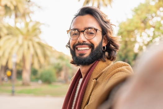 Attractive man with glasses and beard taking a selfie smiling outdoors in the park. Happy smiling student video call. Technology, education, Erasmus and communication concept. Point of view photo.