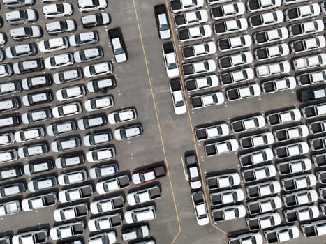 Aerial view of new cars stock at factory parking lot. Above view cars parked in a row. Automotive industry. Logistics business. Import or export new cars at warehouse. Big parking lot at port terminal