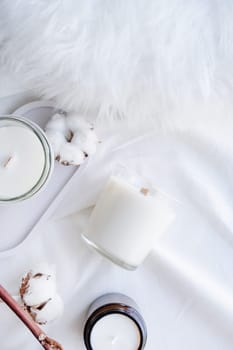 Soy wax aroma candle in white jar on bed with cotton branch. Candle mockup design. Mockup soy wax candle in natural style.