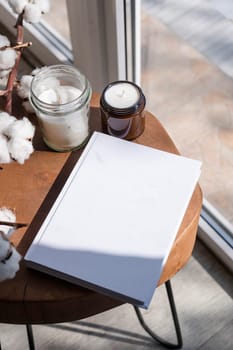 Magazine and book mockup design. Blank magazine on modern wooden table with candles , shadow overlay. Mockup soy wax candle in natural style.