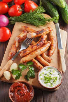 Delicious sausages on a wooden board with various sauces and fresh vegetables on a wooden table. vertical photo