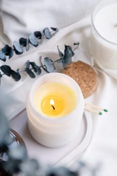 Soy wax aroma candle in white jar on bed with eucalyptus leaves. Candle mockup design. Mockup soy wax candle in natural style.