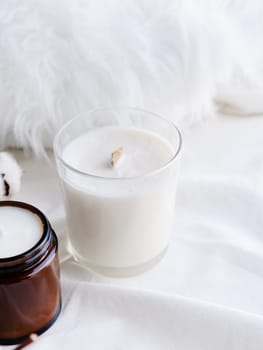 Soy wax aroma candle in white jar on bed with cotton branch. Candle mockup design. Mockup soy wax candle in natural style.