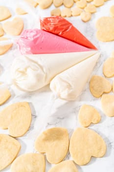 Decorating heart-shaped sugar cookies with pink and white royal icing for Valentine's Day.