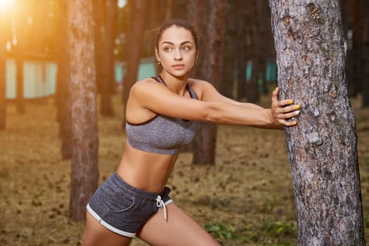 Young woman running outdoors in a city park on. doing warm-up and stretching. with a sun flare