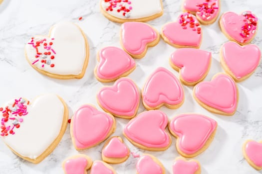 Decorating heart-shaped sugar cookies with pink and white royal icing for Valentine's Day.