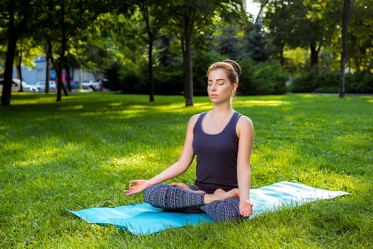 Meditating woman in meditation in city park in yoga pose. Girl relaxing with serene relaxed expression outside in summer. Beautiful young Caucasian female model.