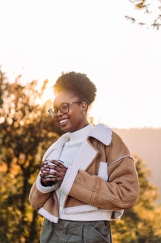 young african woman smiling happy in nature with a mug of hot drink in hand, concept of morning bliss and wilderness lifestyle, copy space for text